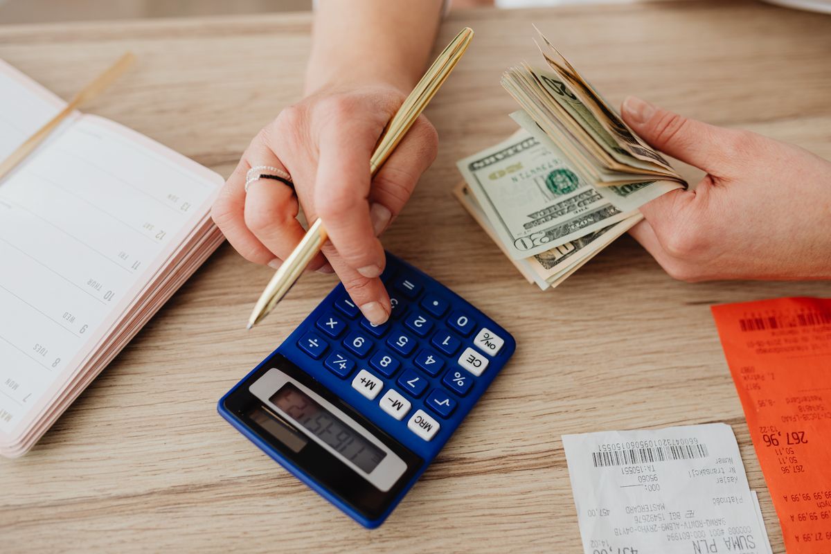 Someone working out a budget with a calculator, cash and receipts spread on a table
