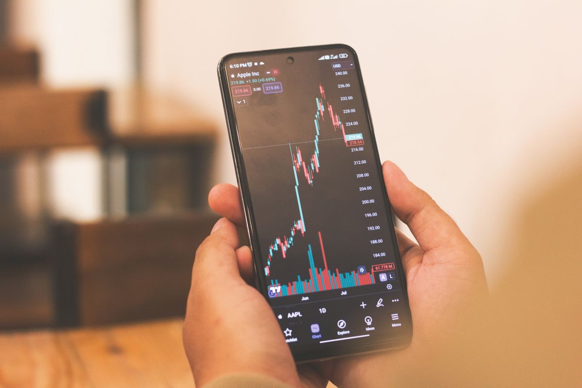 A phone held in one hand showing a stock price chart