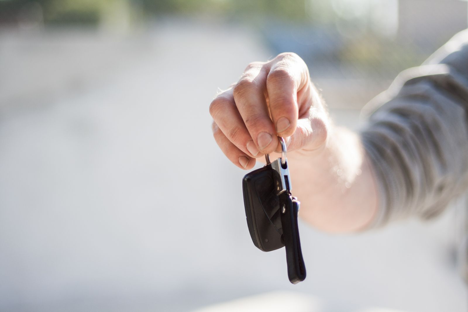 A hand holding out a car key fob against a blurred outdoor background