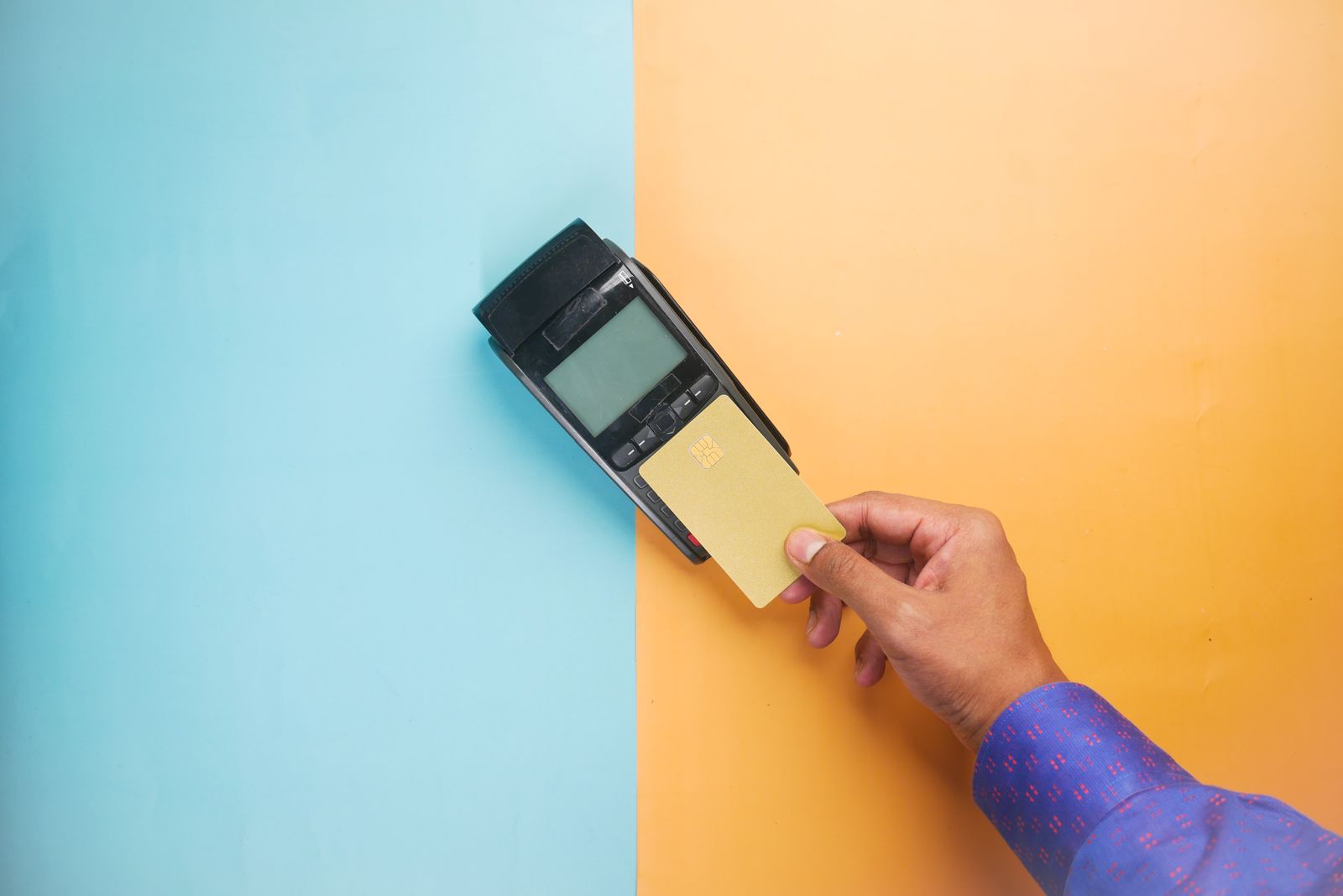 A hand tapping a gold card against a payment terminal on a two-tone blue and orange background