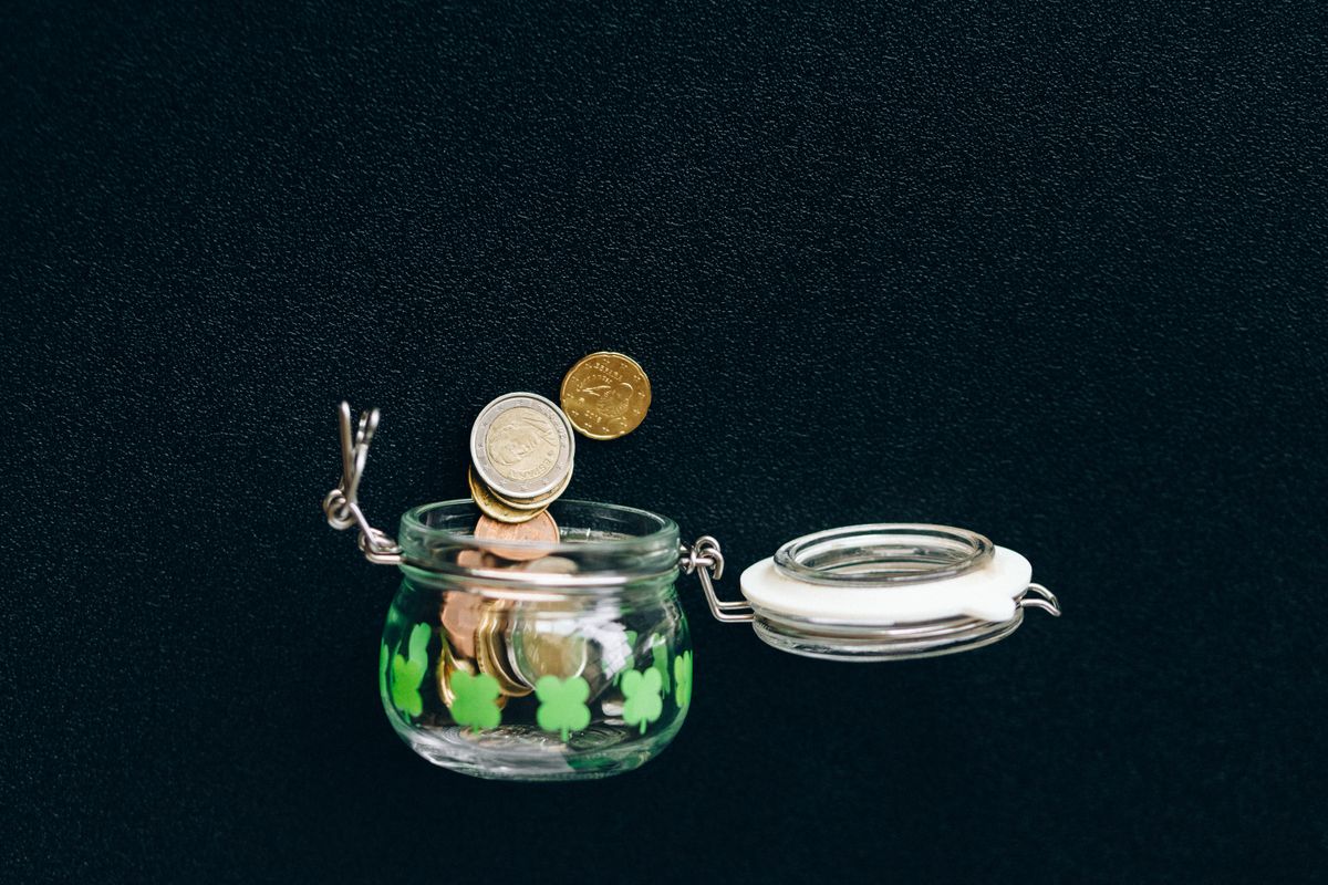 Coins dropping into a small glass jar against a dark background