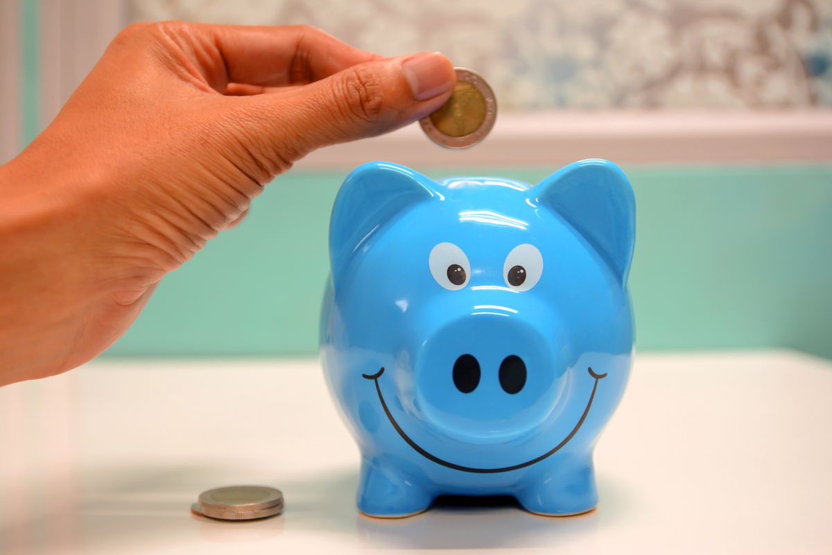 A hand dropping a coin into a smiling blue piggy bank