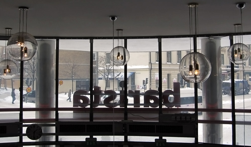 A view out of a cafe window onto a snowy street, the barista sign seen from behind