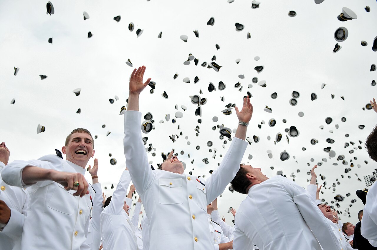Naval Academy graduates in dress whites throwing their caps into the air