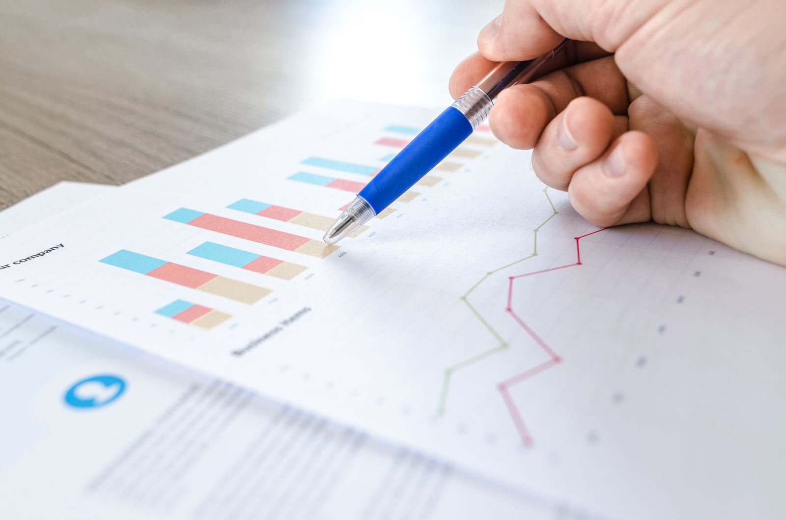 A hand holding a pen over a printed page of colorful bar and line charts
