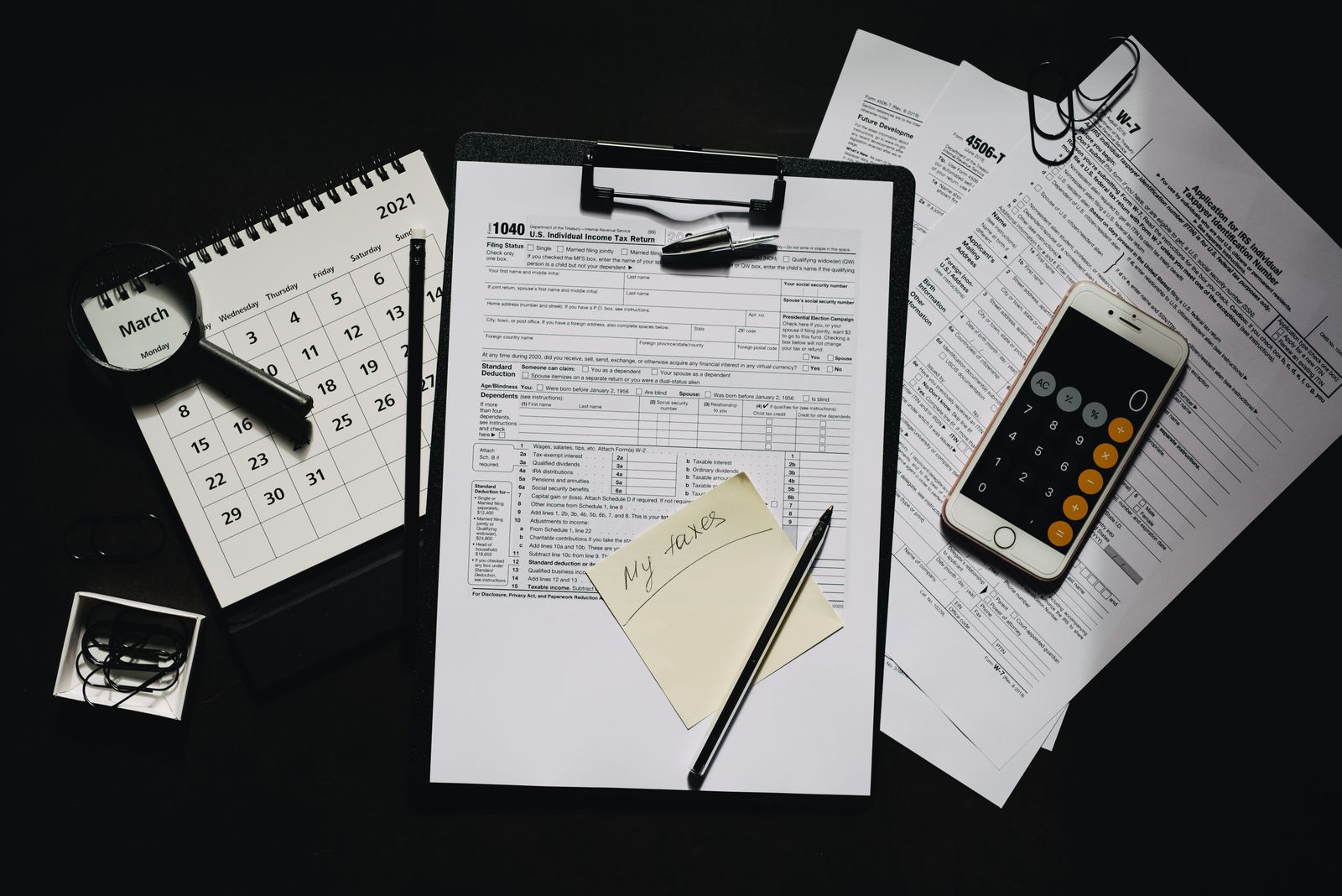 A 1040 tax form on a clipboard next to a calculator, calendar, and magnifying glass