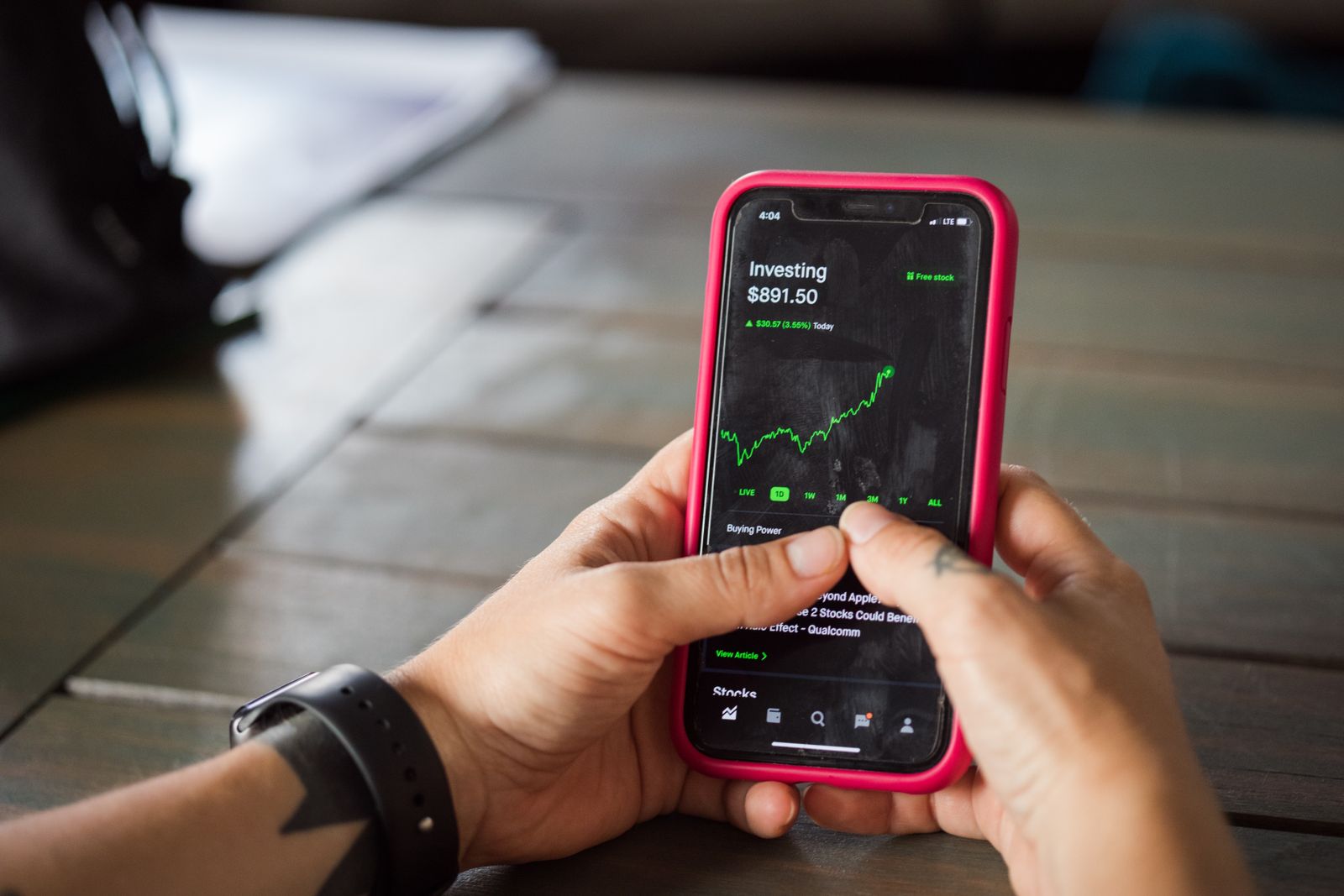 Hands holding a smartphone showing an investing app with a rising green stock chart