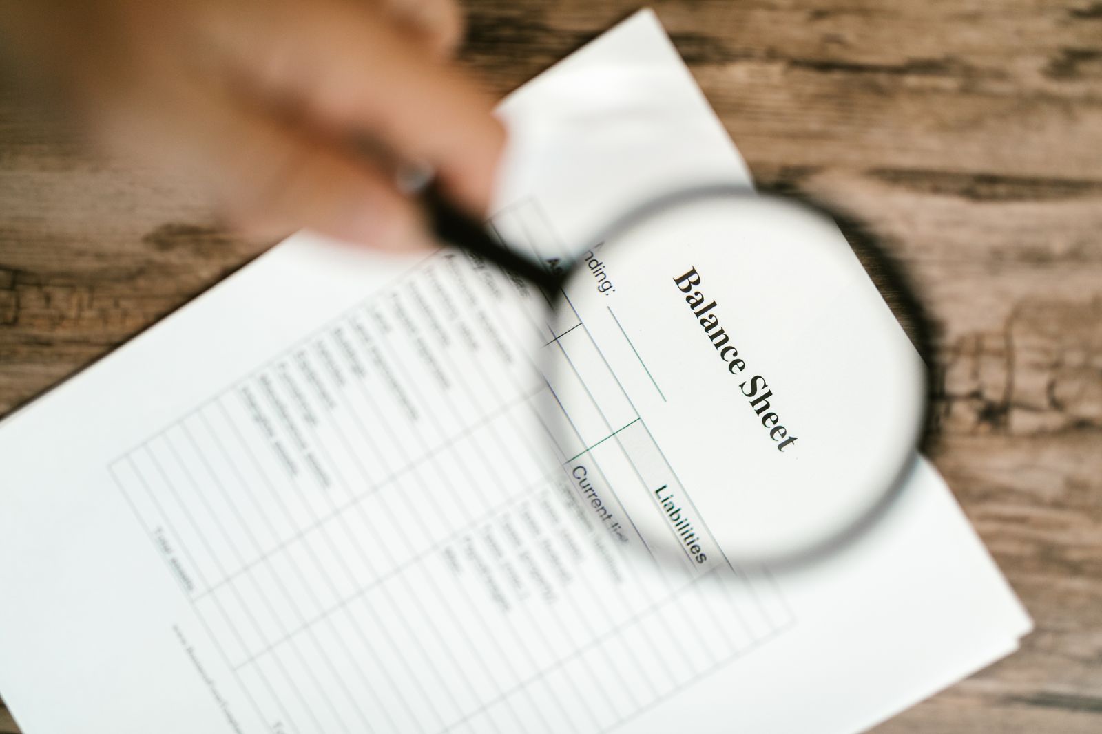 A magnifying glass held over a document titled Balance Sheet on a wooden table