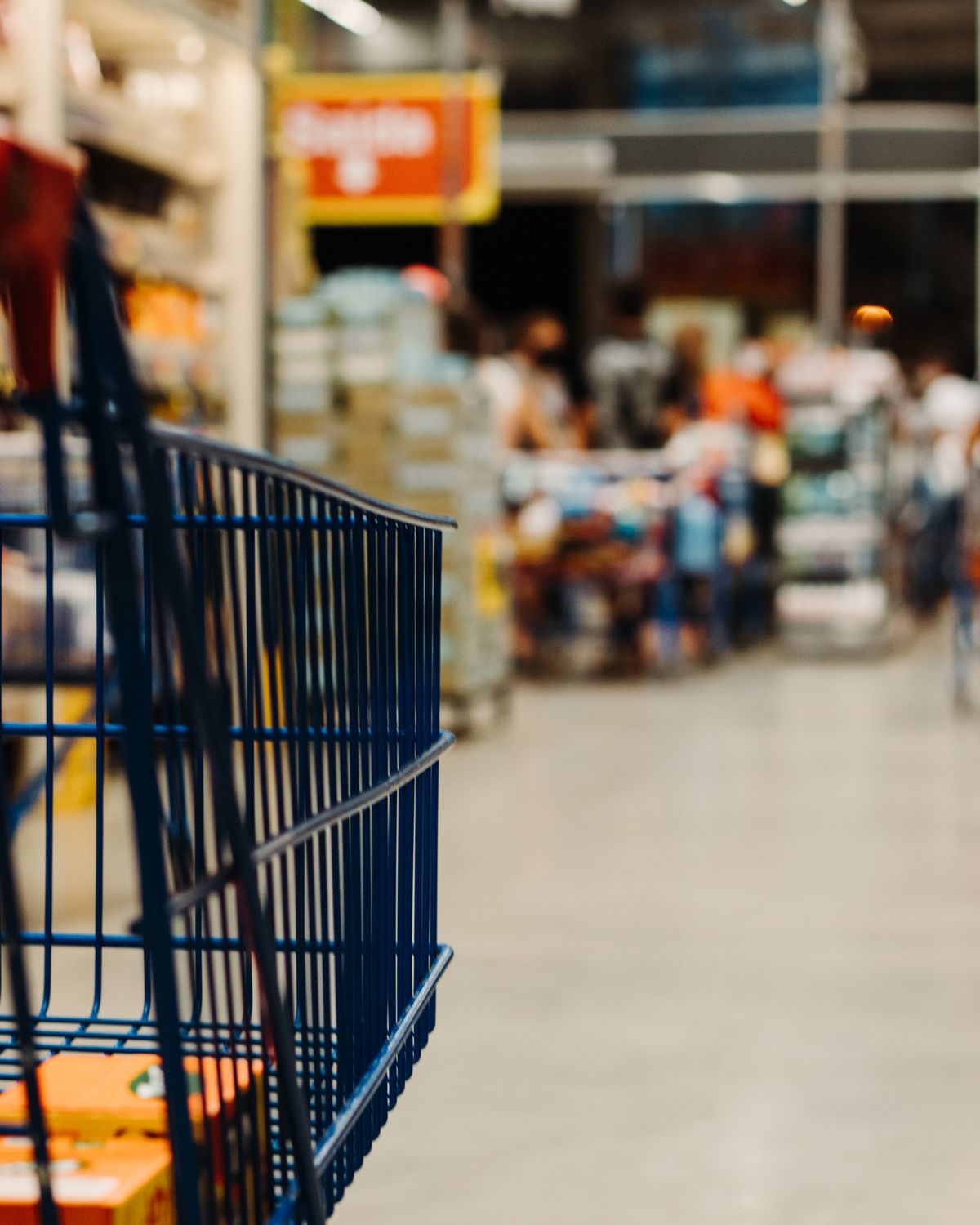 A shopping cart in a supermarket aisle with shoppers blurred behind it