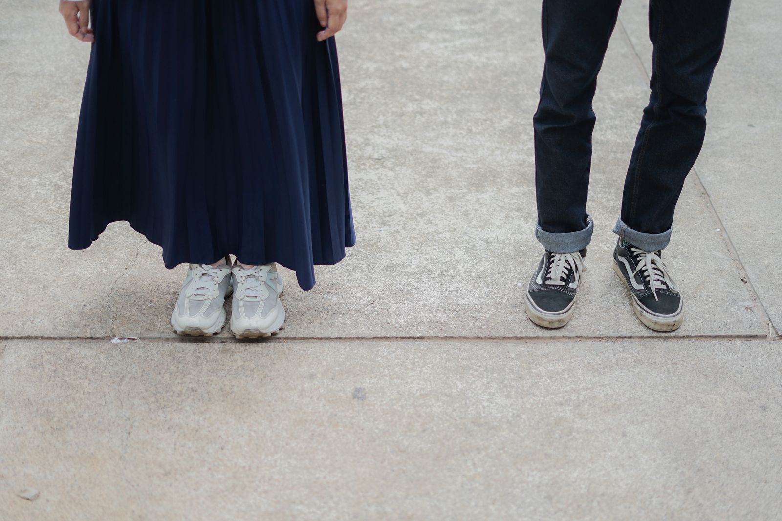 Two people standing on a sidewalk showing only their sneakers and lower legs
