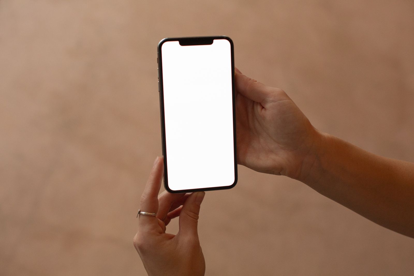 A hand holding up a smartphone with a blank white screen against a warm background