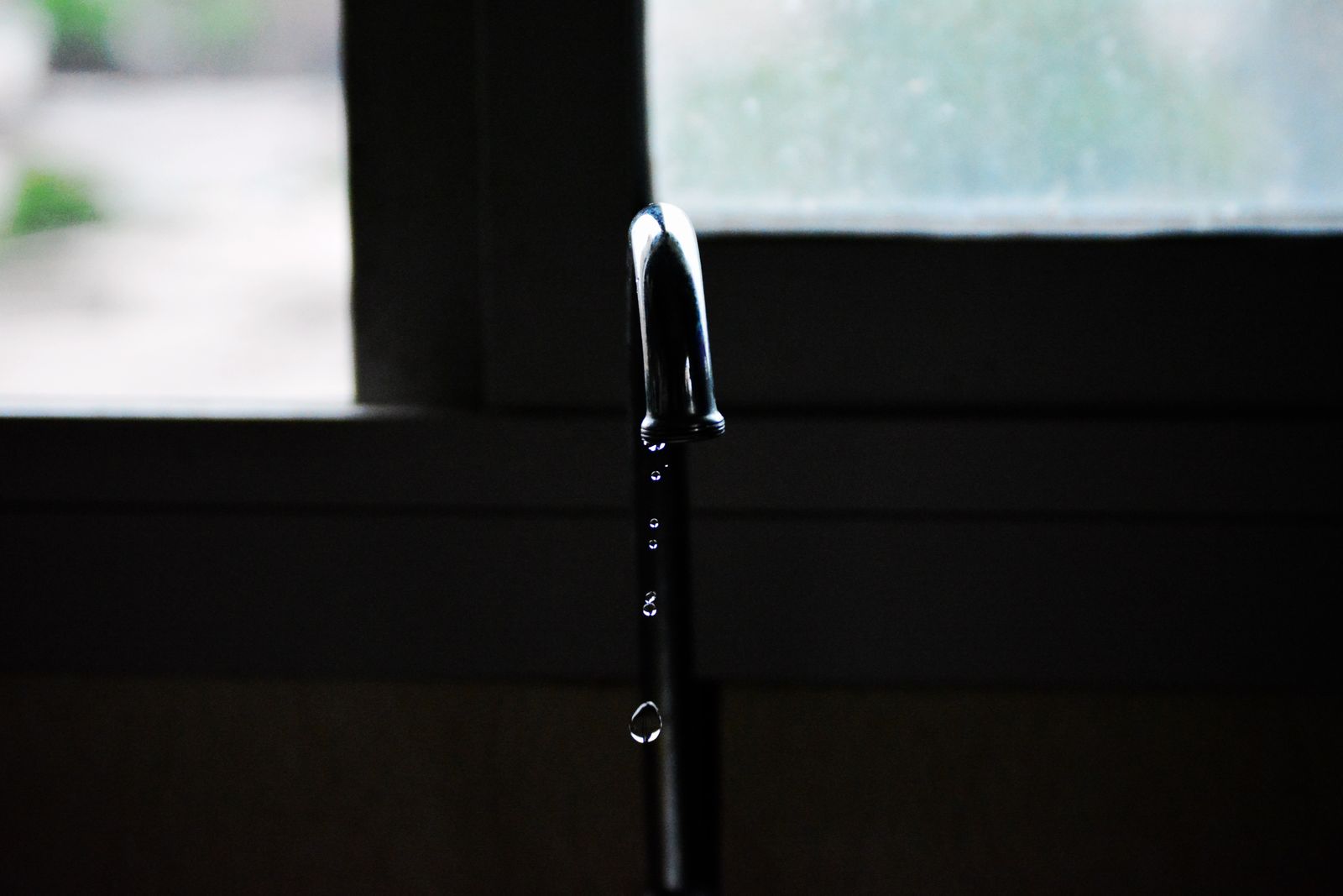 A tap slowly dripping water in front of a dark window