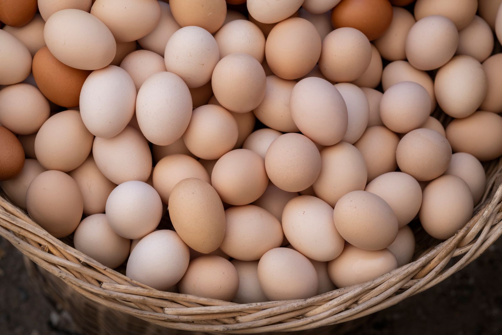 A wicker basket completely filled with brown and white eggs viewed from above