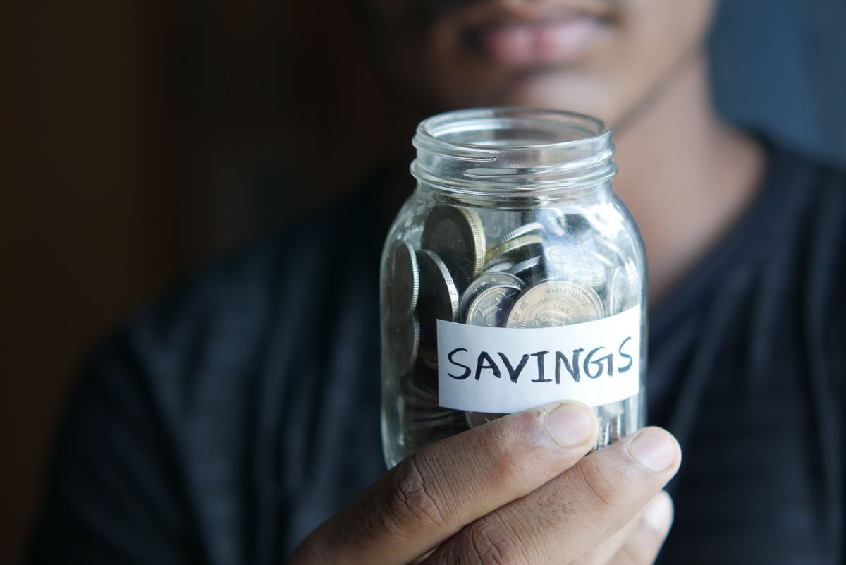 A person holding a glass jar of coins labelled savings