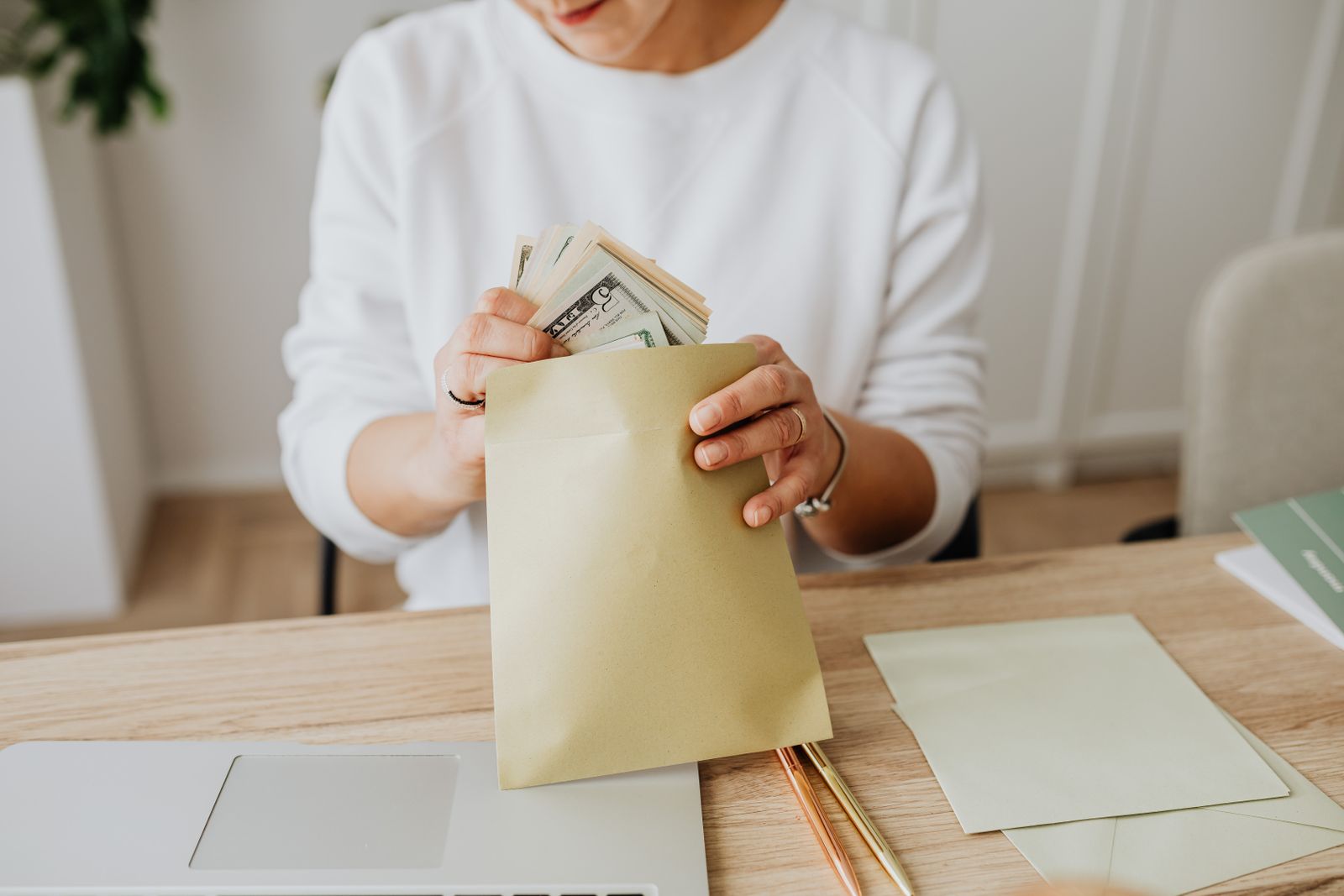 Hands tucking a stack of cash into a kraft paper envelope at a desk