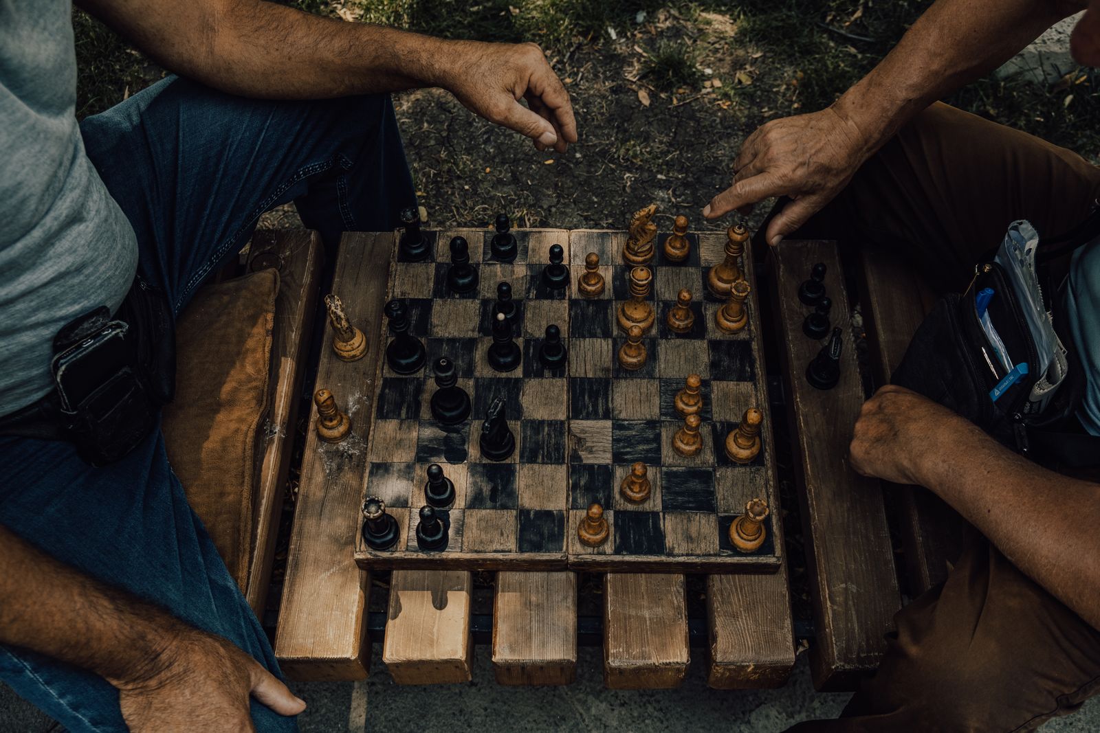 Overhead view of two people's hands moving pieces on a wooden chess board outdoors
