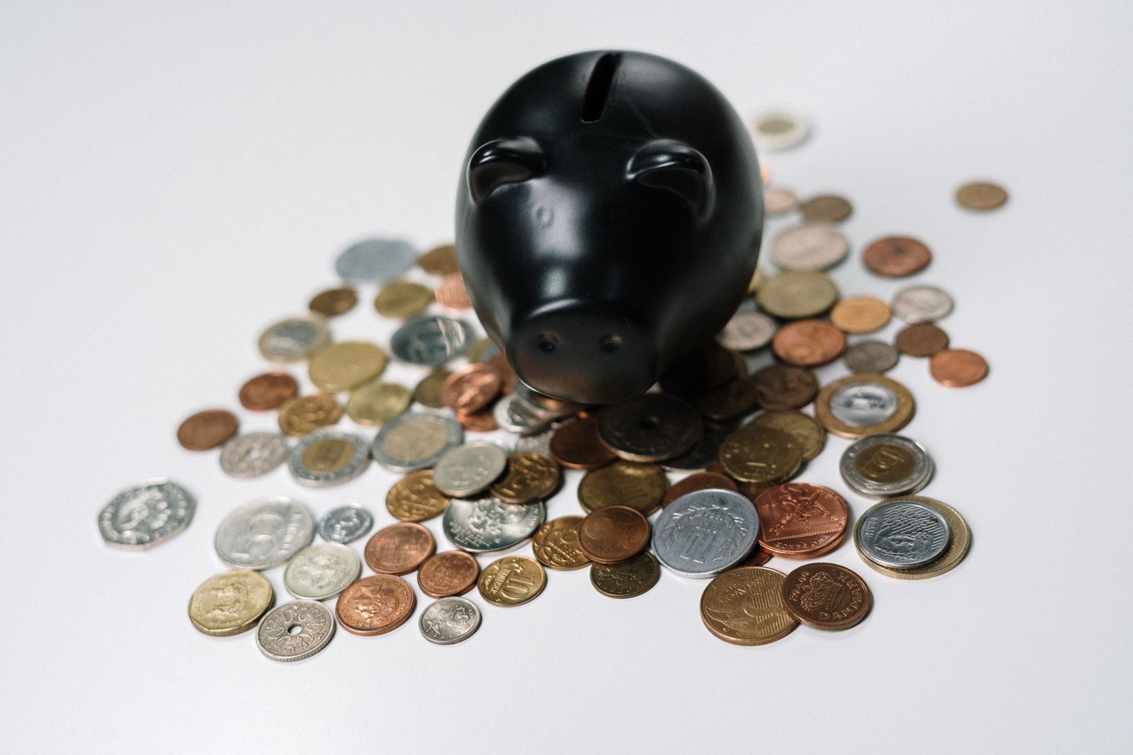 A black piggy bank surrounded by a scattered pile of coins