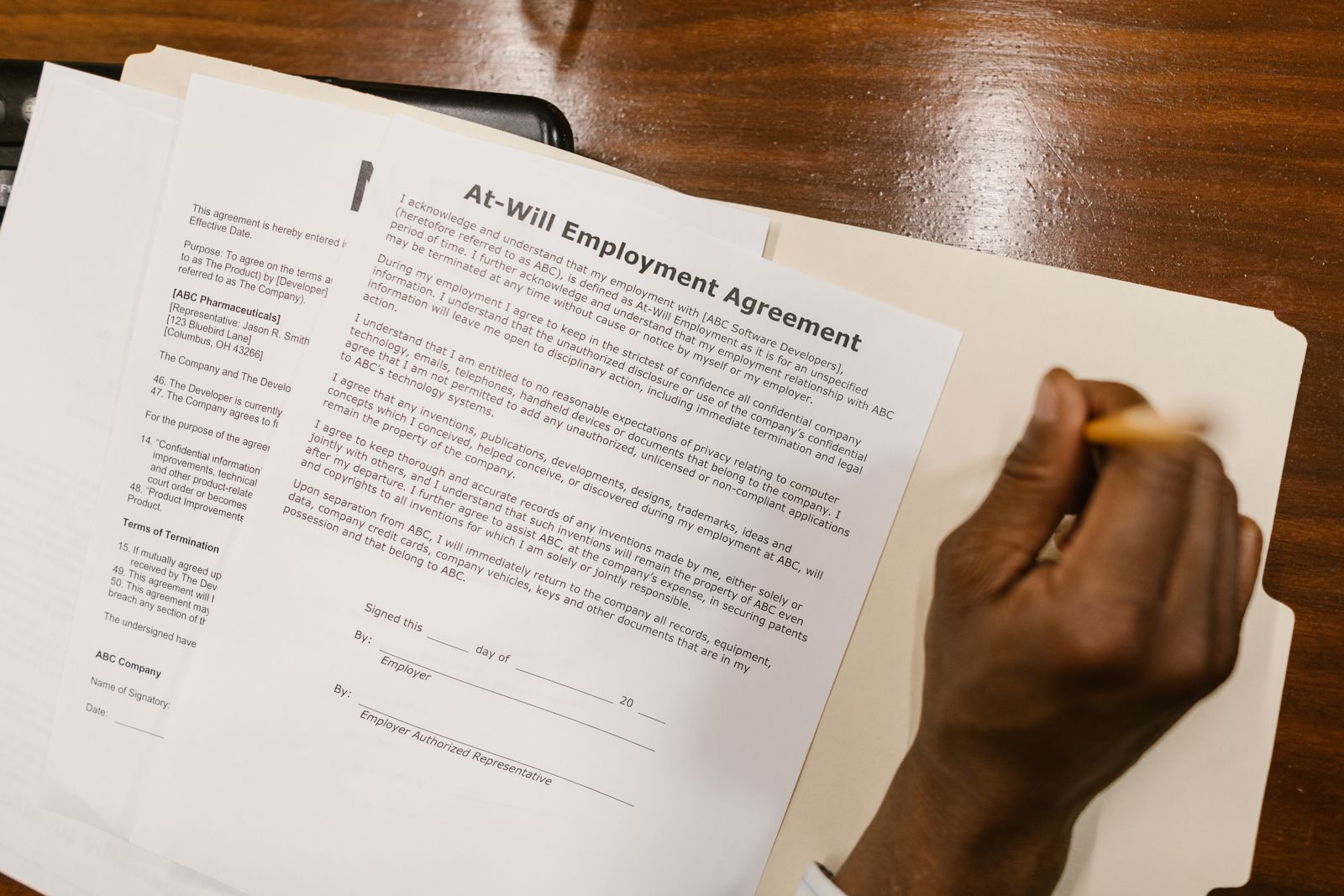 A hand holding a pencil over an at-will employment agreement on a desk