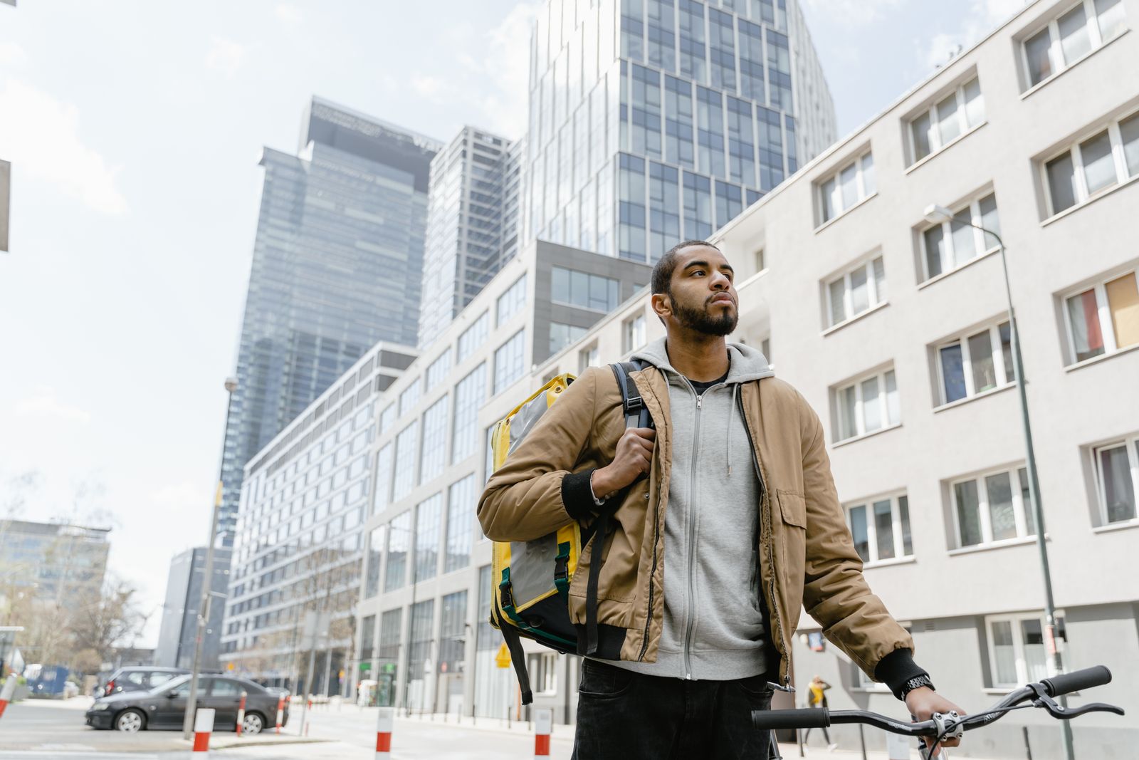 A delivery courier with a bike and thermal bag standing among city high-rises