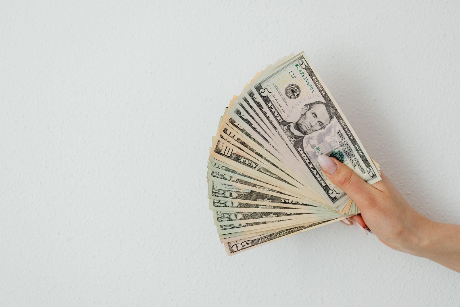 A hand holding a fanned-out spread of US dollar bills against a plain wall