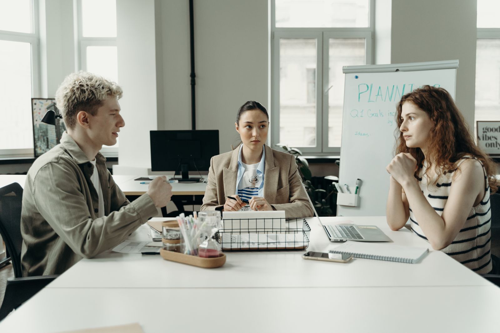 Three coworkers talking around a table in an office with a planning whiteboard behind them