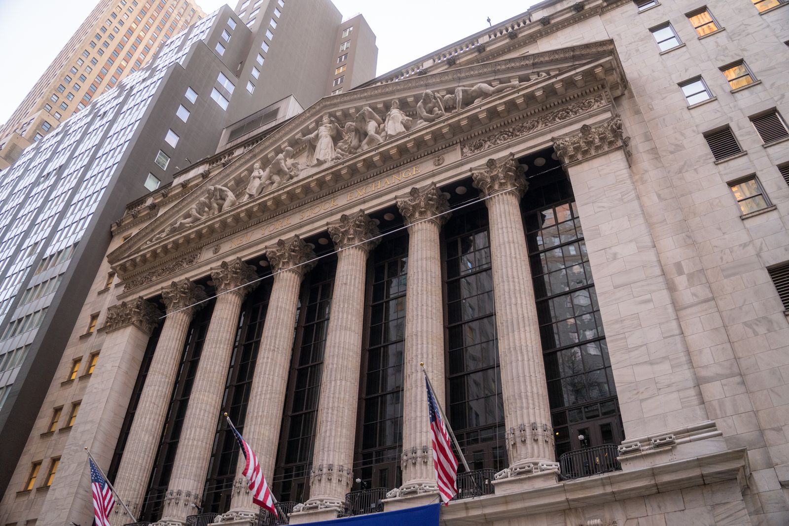 Low angle view of the New York Stock Exchange facade with its carved pediment and American flags