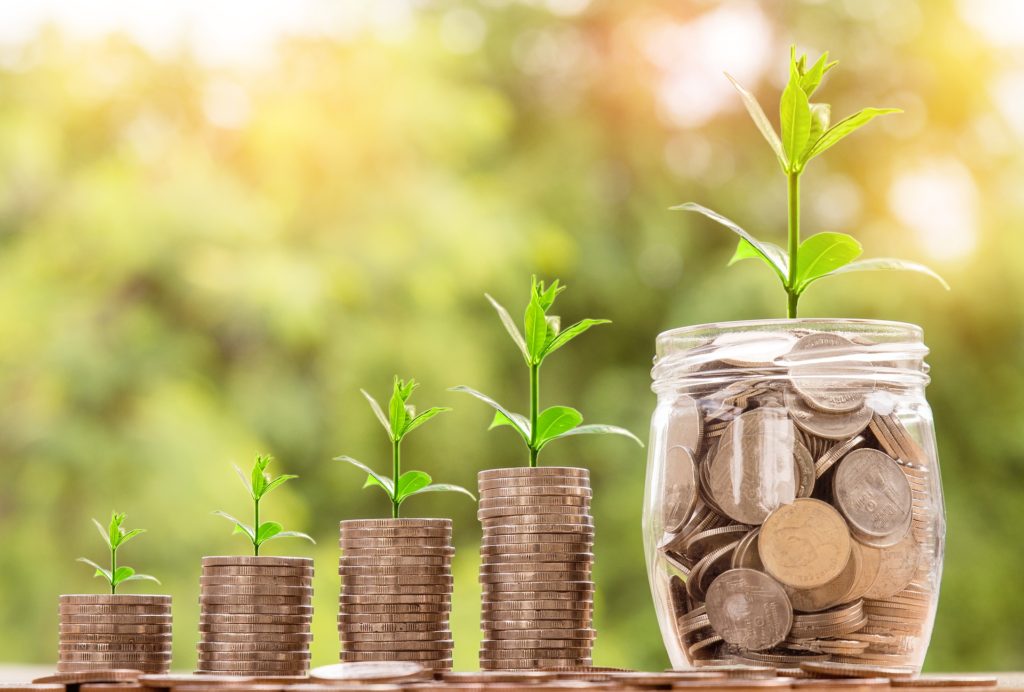 Four rising stacks of coins with seedlings growing from them, beside a jar of coins