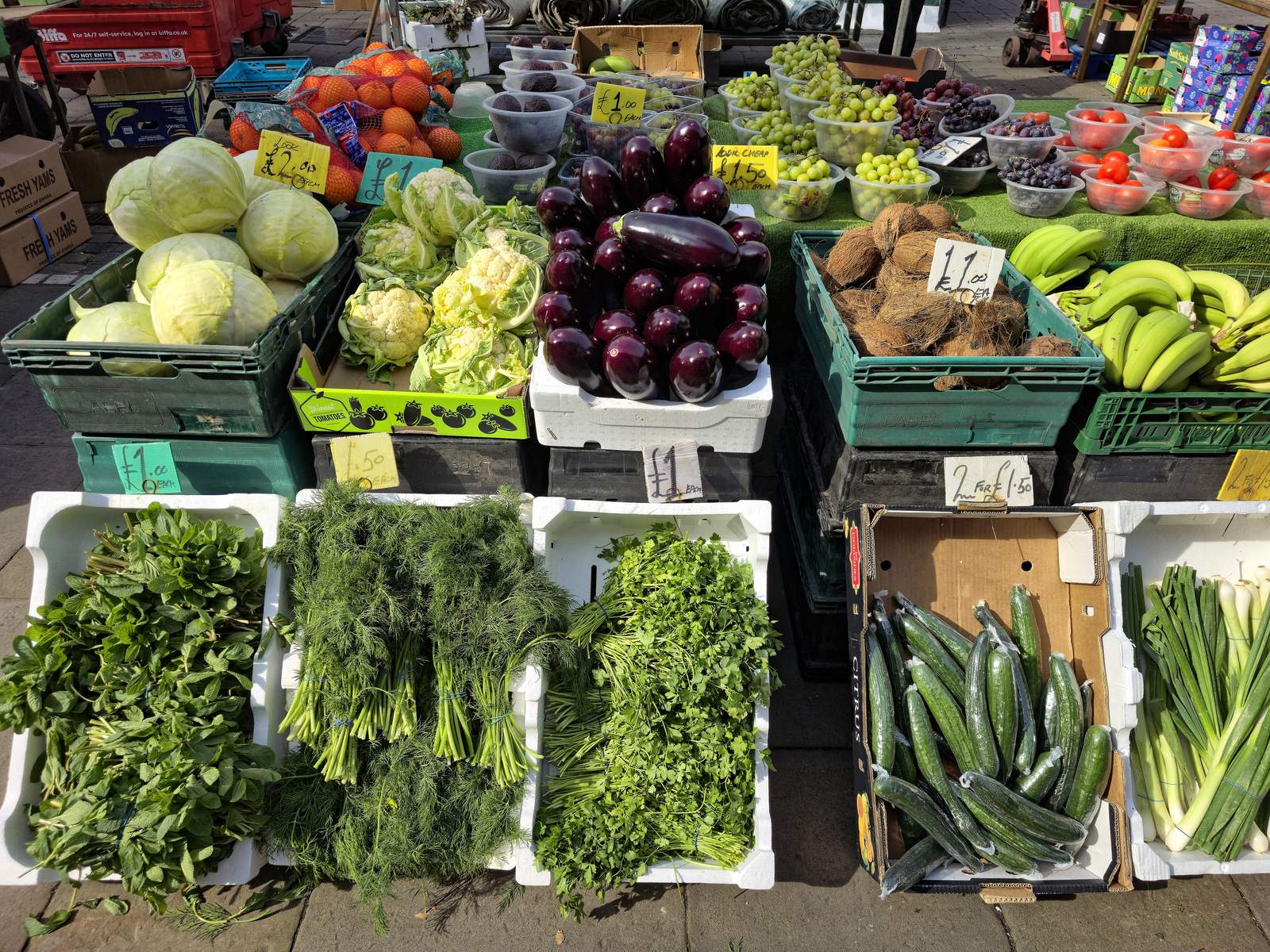 Crates of cabbages, eggplants, bananas and herbs at an outdoor market stall