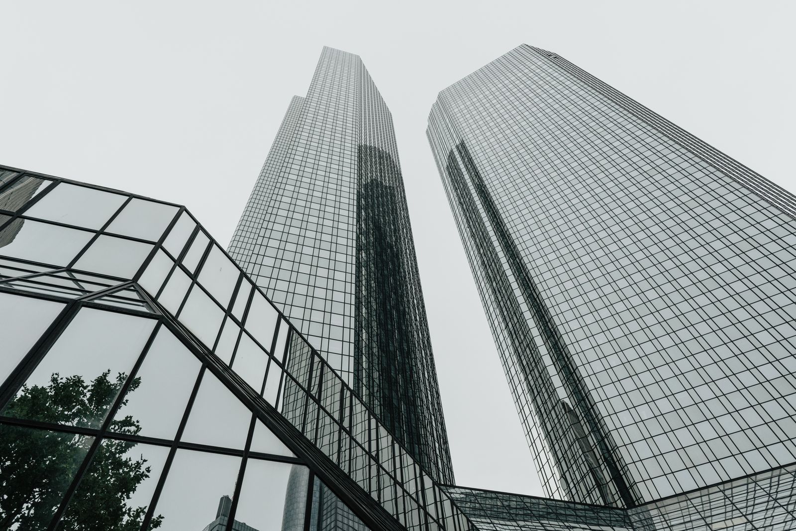 Looking straight up at two glass office skyscrapers against an overcast sky