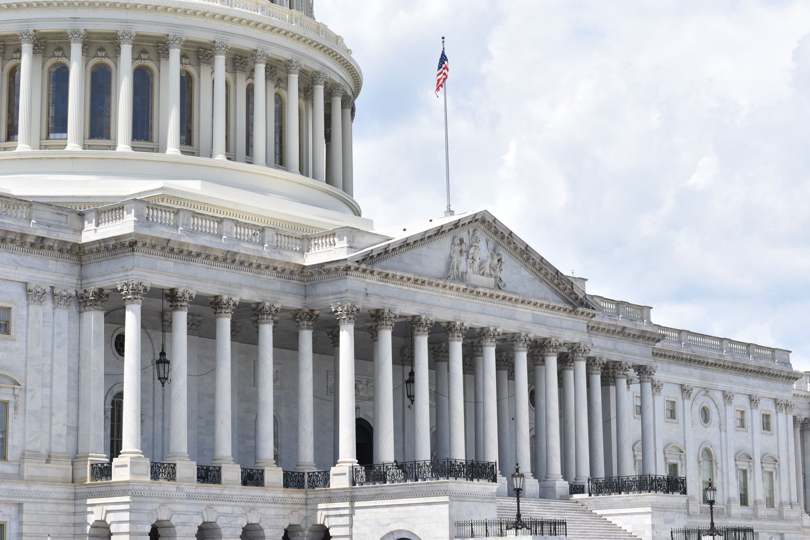 The dome and columned facade of the US Capitol building with an American flag flying