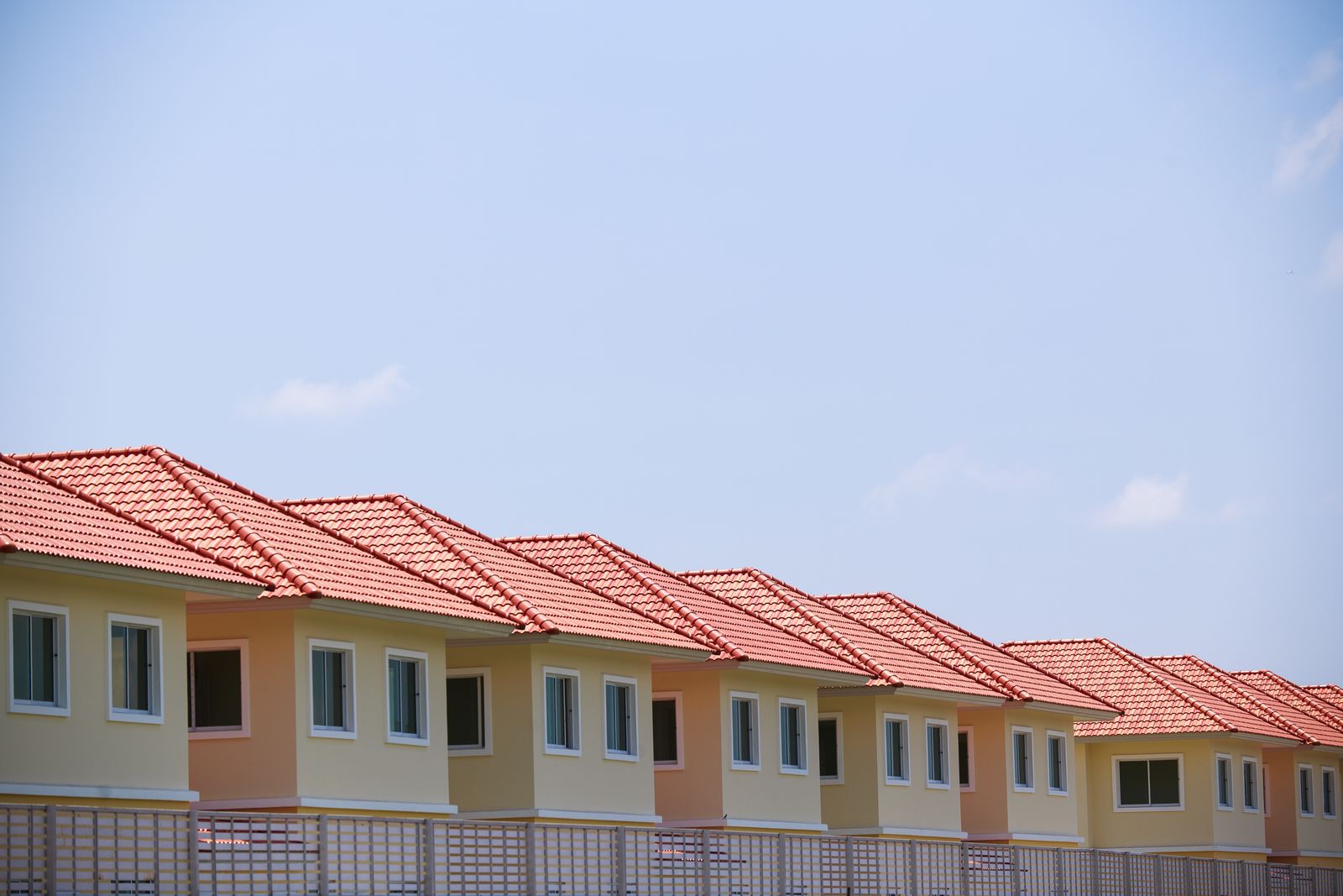 A line of identical suburban houses with red tiled roofs and beige exteriors under a clear sky