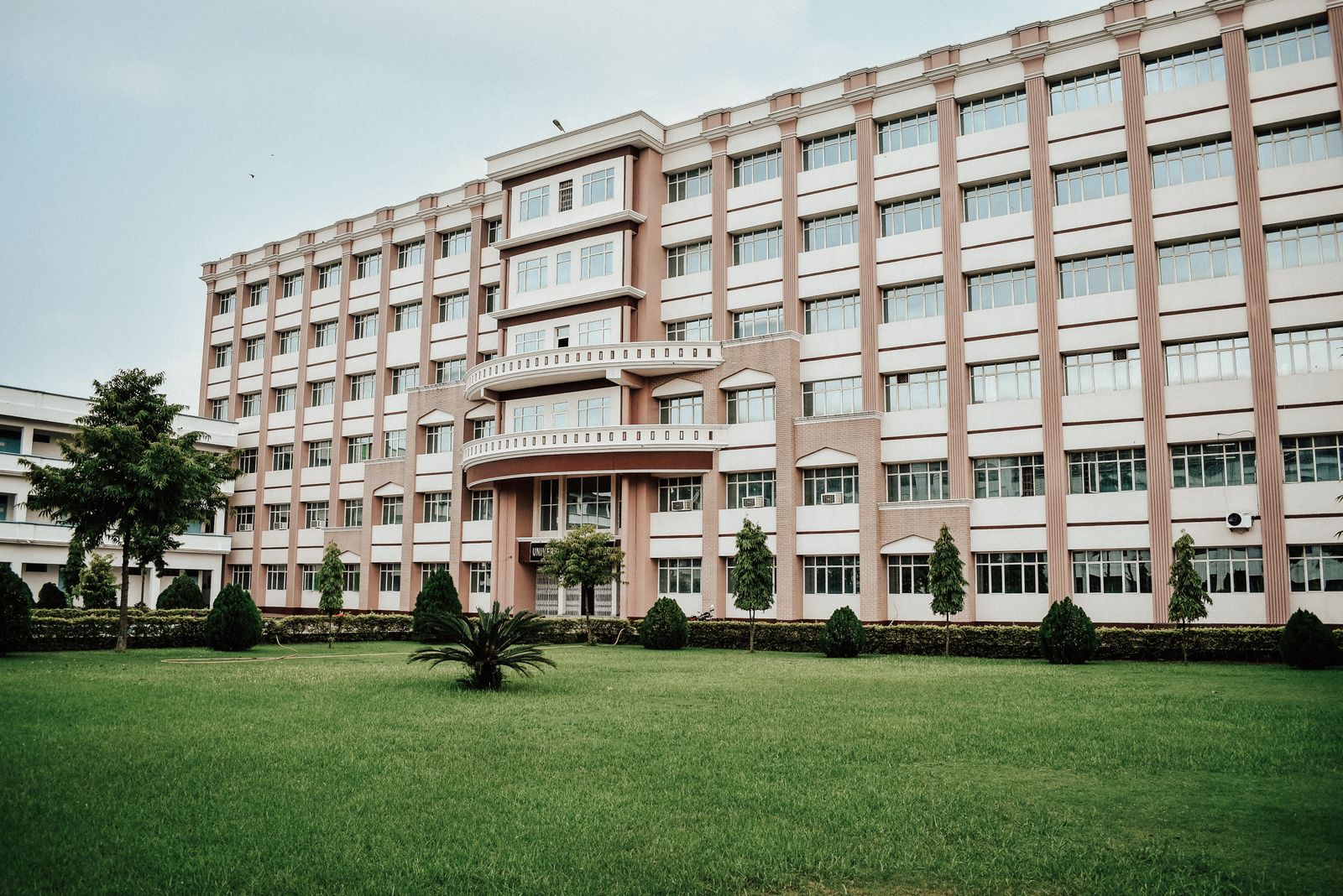 A large multi-story university building with a wide well-maintained lawn in front